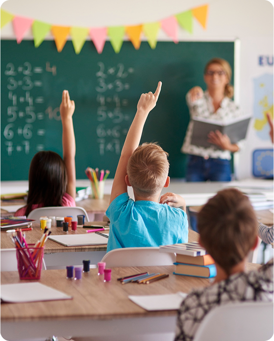 Classroom with children raising hands and teacher at chalkboard